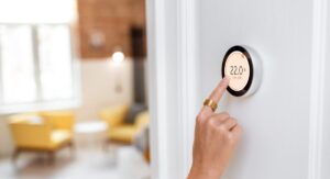 Hand adjusting a digital smart thermostat to 22 degrees Celsius in a bright living room