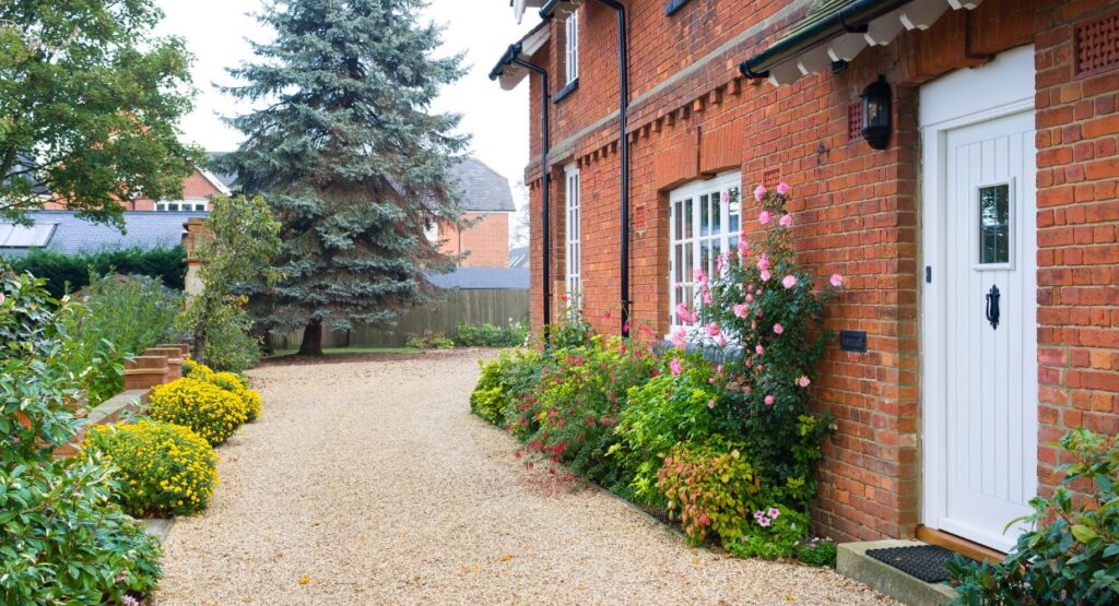 Exterior of a red brick UK home with a tidy gravel path and blooming garden, representing Hunters’ 2025 landlord guide on property repairs, inspections and compliance.