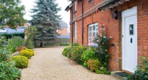 Exterior of a red brick UK home with a tidy gravel path and blooming garden, representing Hunters’ 2025 landlord guide on property repairs, inspections and compliance.