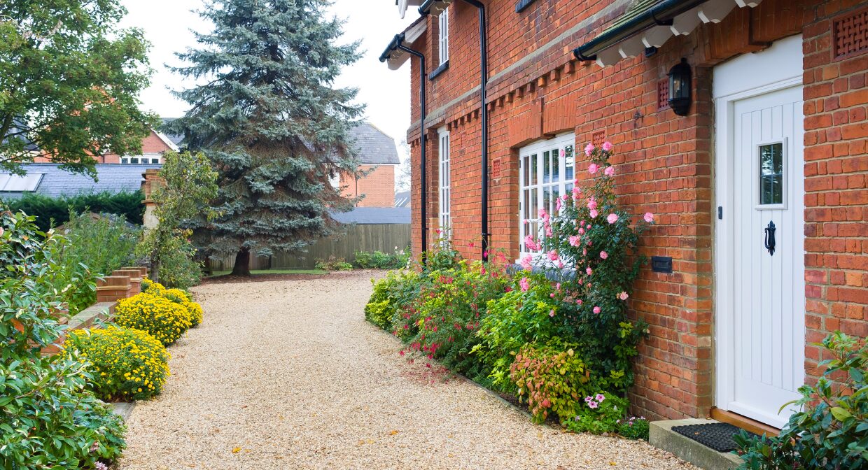 Exterior of a red brick UK home with a tidy gravel path and blooming garden, representing Hunters’ 2025 landlord guide on property repairs, inspections and compliance.