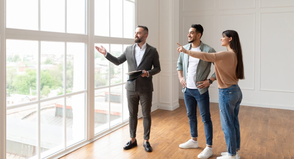 A professional estate agent showing a bright modern property to a couple during a viewing, representing landlord compliance, inspections and professional property management.