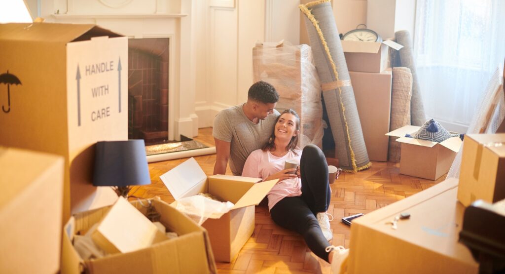 A young couple sitting on the floor surrounded by moving boxes while unpacking in their new home, representing landlords, tenants and the importance of legal compliance in the lettings process.