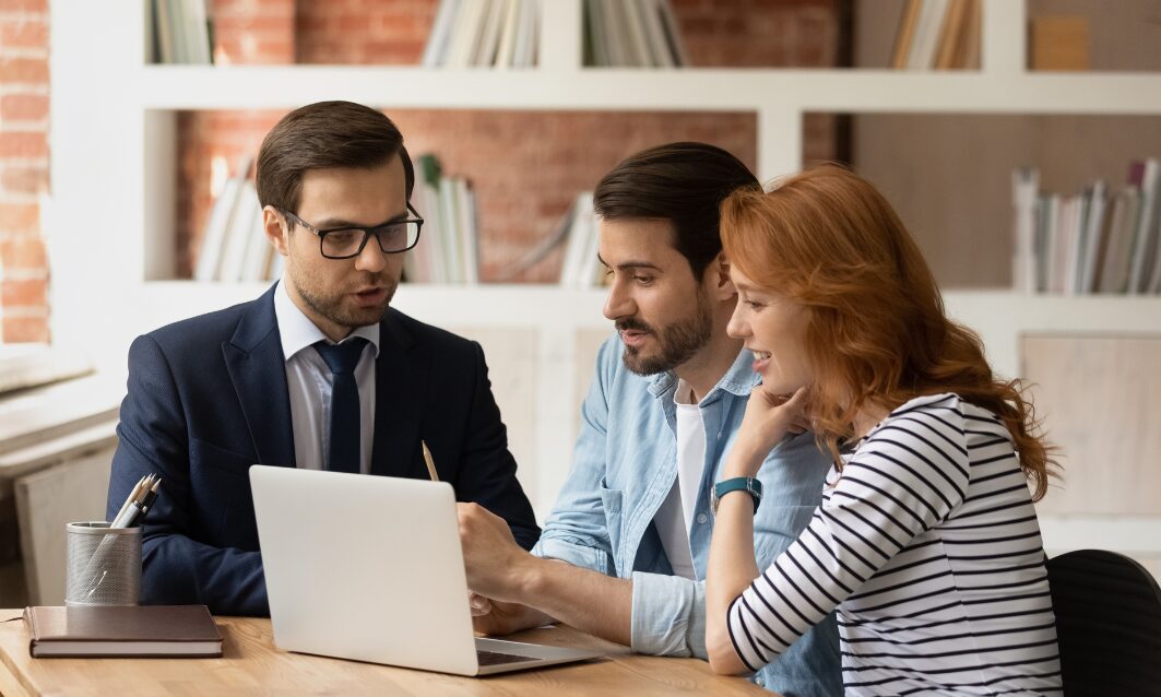 Professional advisor explaining tenancy changes to a couple during a meeting with a laptop.