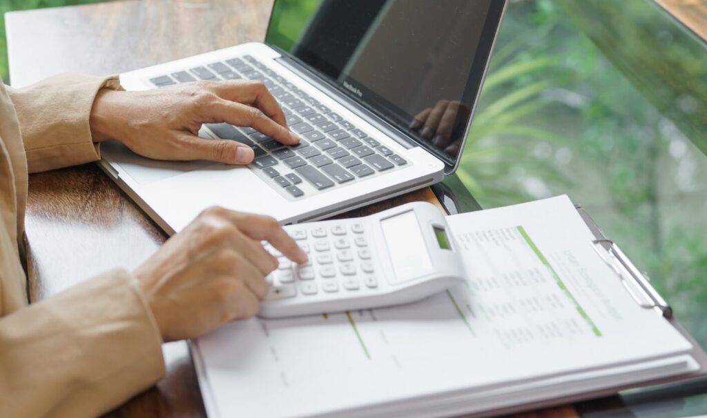 Person calculating landlord expenses using a laptop and calculator while reviewing property cost documents.