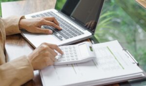 Person calculating landlord expenses using a laptop and calculator while reviewing property cost documents.