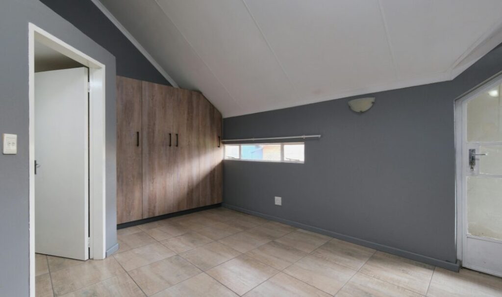 An empty, well maintained room with grey walls, tiled flooring, and built in wooden cupboards, representing a mortgage free home after inheritance and decisions about next steps.