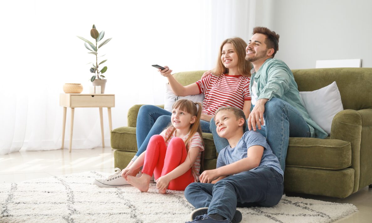 Happy family sitting together on a living room floor watching TV in a bright, modern home.