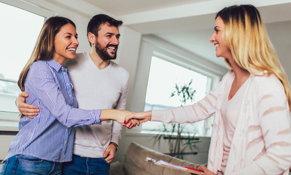 A landlord shaking hands with a couple inside a bright rental property