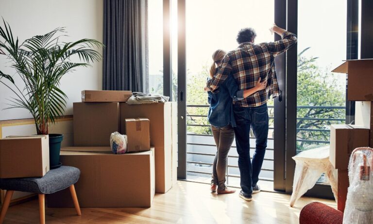 Couple standing in a new home surrounded by moving boxes looking out at view