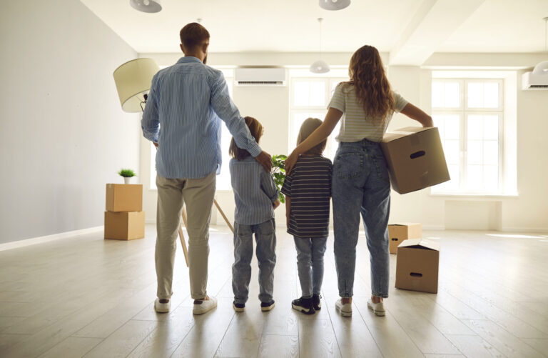 family standing in bright empty home with moving boxes symbolising buying a house near
