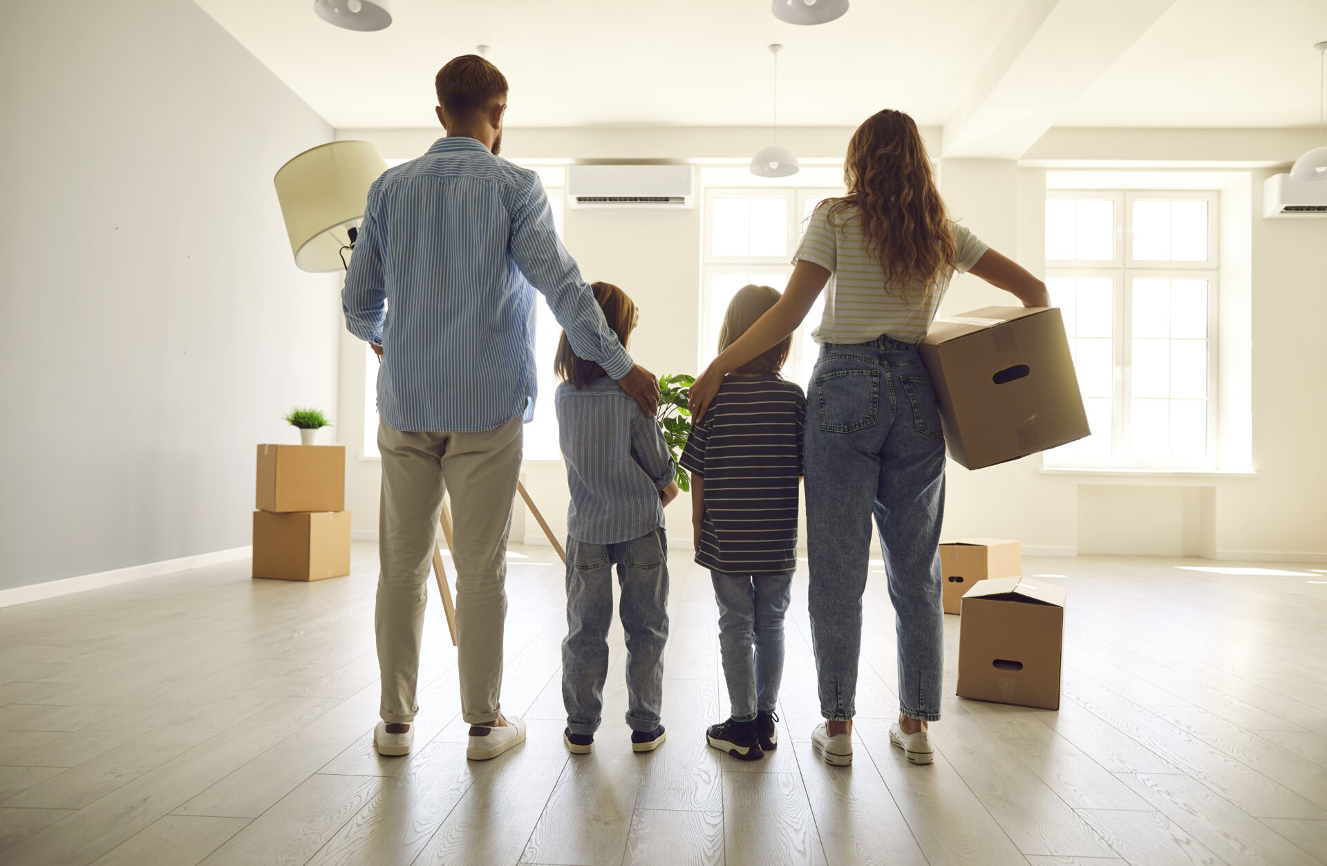 family standing in bright empty home with moving boxes symbolising buying a house near