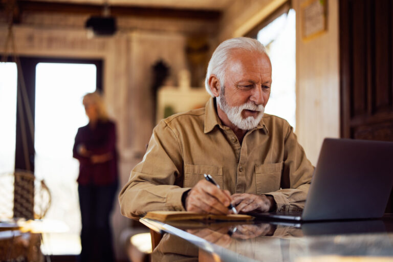 older man reviewing property investment notes on laptop at home