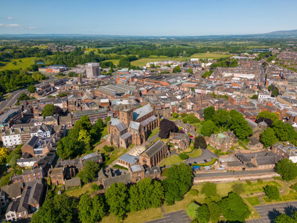 Drone view overlooking Carlisle city centre and Carlisle Cathedral surrounded by residential neighbourhoods and green countryside.