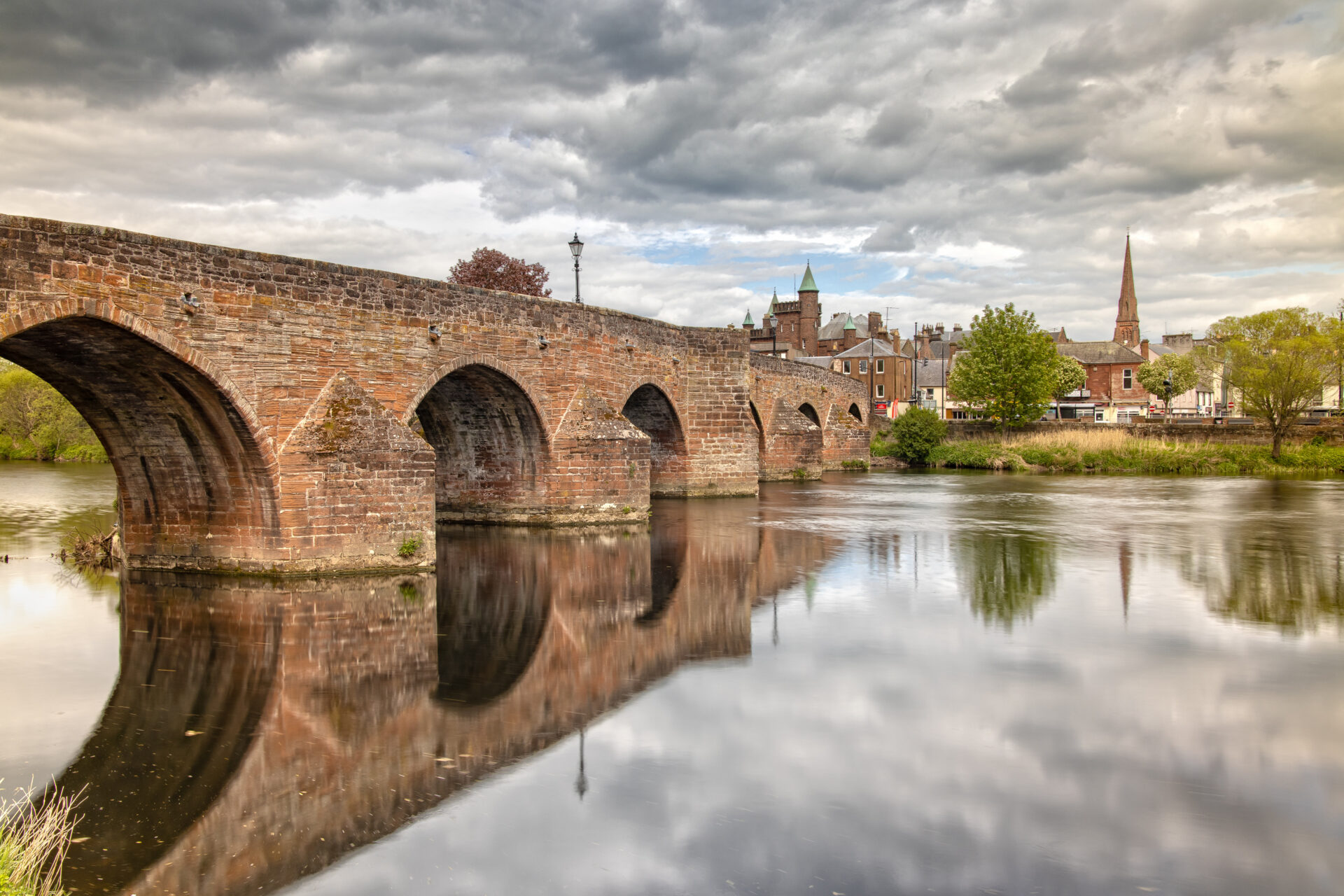 Historic stone bridge over the River Nith in Dumfries with riverside homes and town skyline