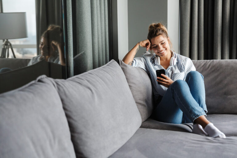 Woman sitting on a sofa using her phone and laptop, representing buyers researching homes in Carlisle.