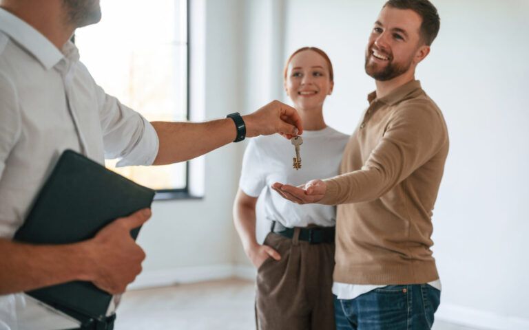 Estate agent handing keys to a smiling tenant couple inside a rental property, reflecting the process of renting a home in Leeds.