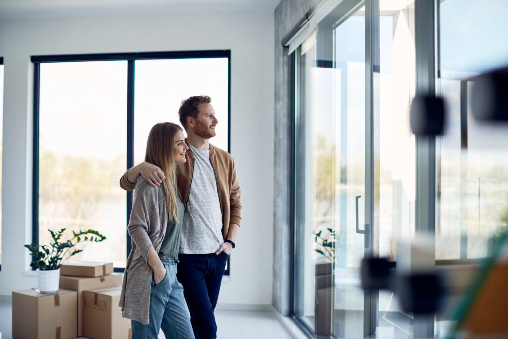 Couple standing in a bright modern home with moving boxes, reflecting the lifestyle appeal and buyer demand for homes in Stanmore.