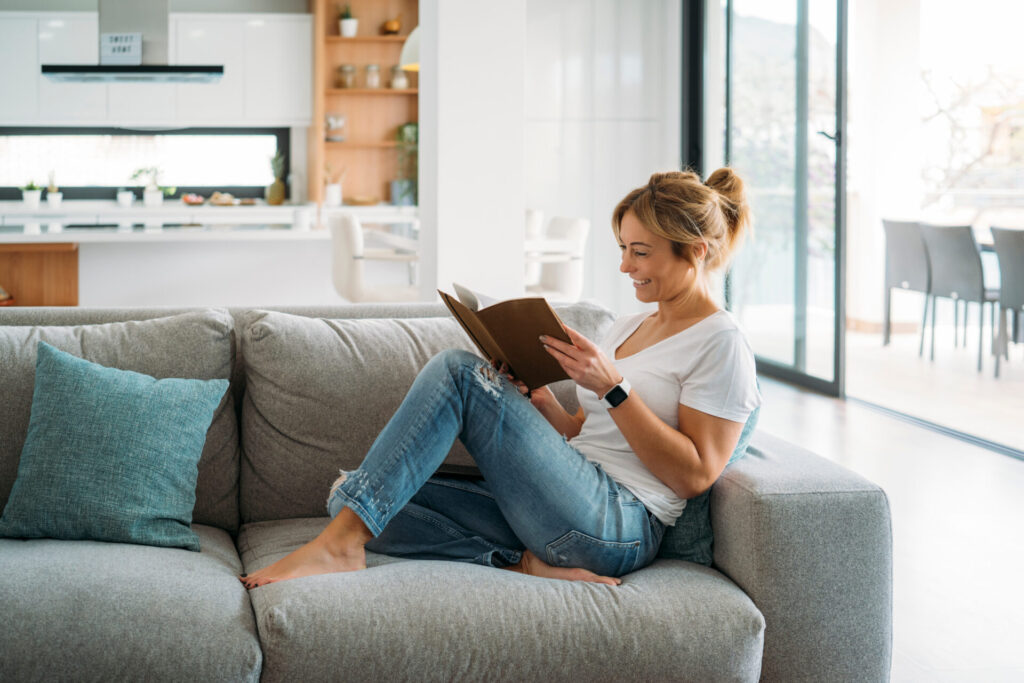 Woman relaxing on a sofa reading a book in a bright modern home, representing the peaceful lifestyle and residential appeal of Boley Park WS14.