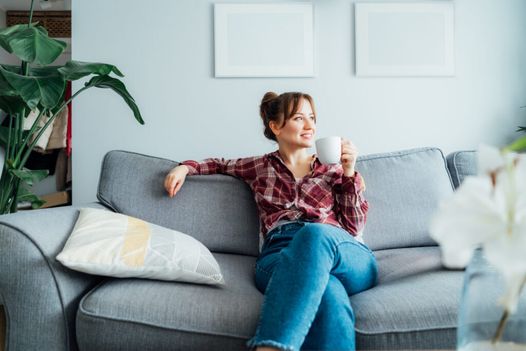 Woman relaxing on a sofa with a cup of coffee in a bright modern home, representing the peaceful lifestyle and residential appeal of Heathhall DG1.