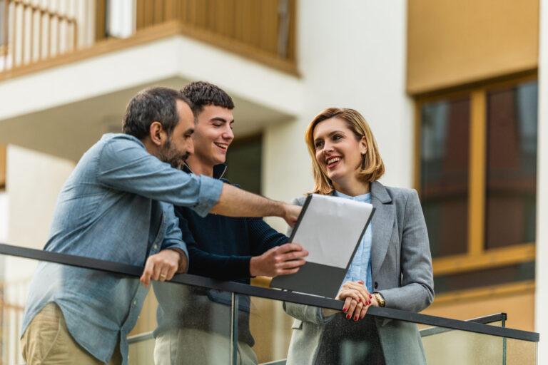 Property agent discussing documents with two clients on a balcony