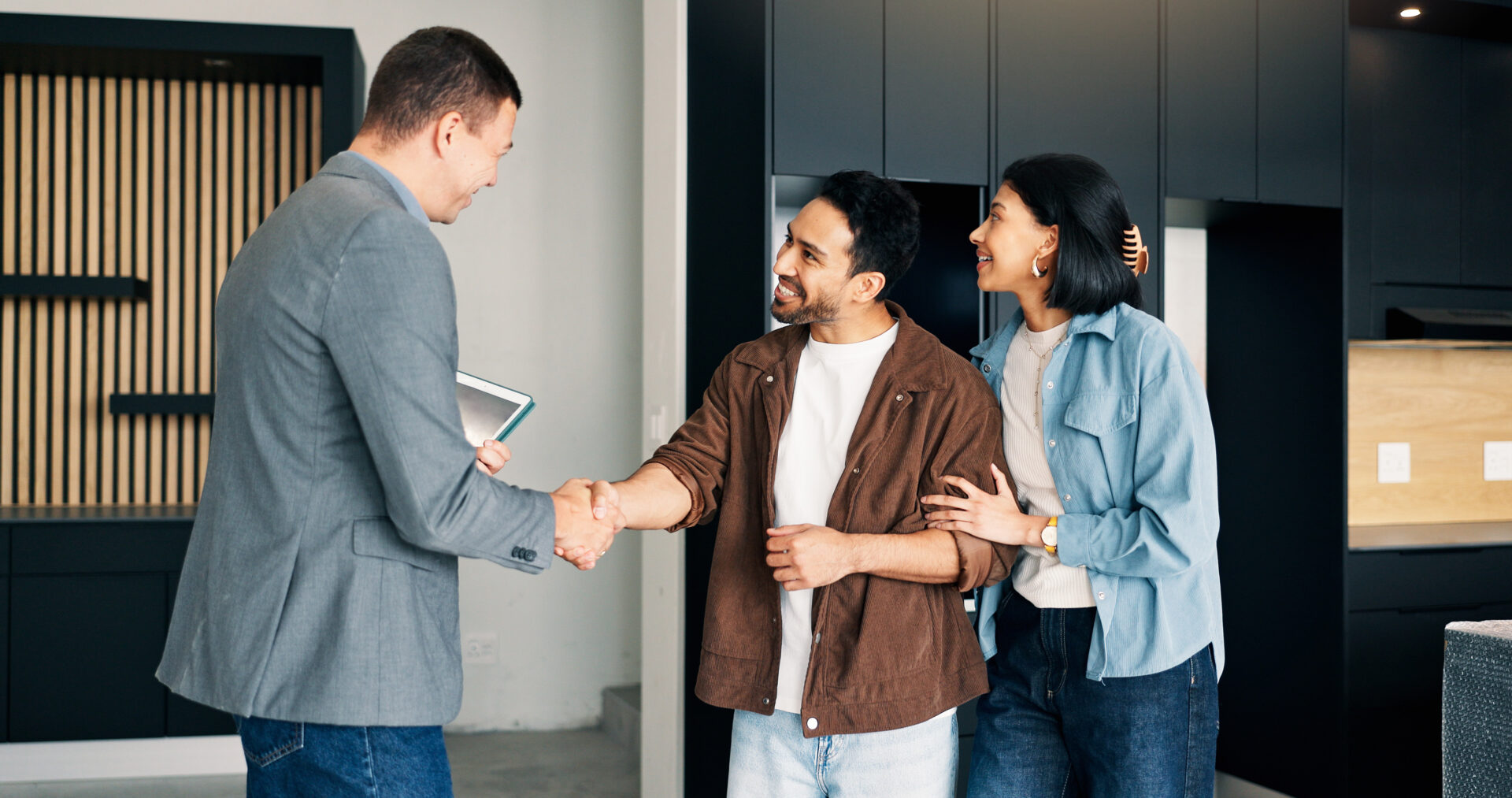 Property agent shaking hands with a couple inside a modern kitchen