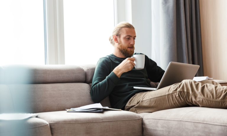 Man sitting on a sofa with a laptop and coffee working through property costs, reflecting the buy-versus-rent comparison between Annan and Carlisle.