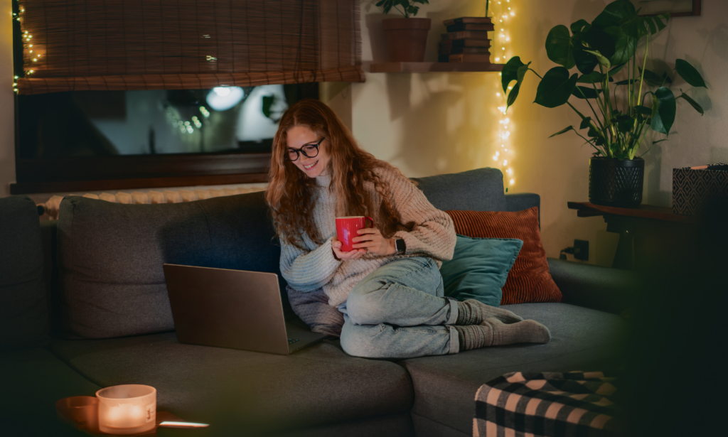 Young woman relaxing on a sofa researching properties on a laptop in the evening, reflecting a first-time buyer learning about LBTT and Home Reports in Dumfries.