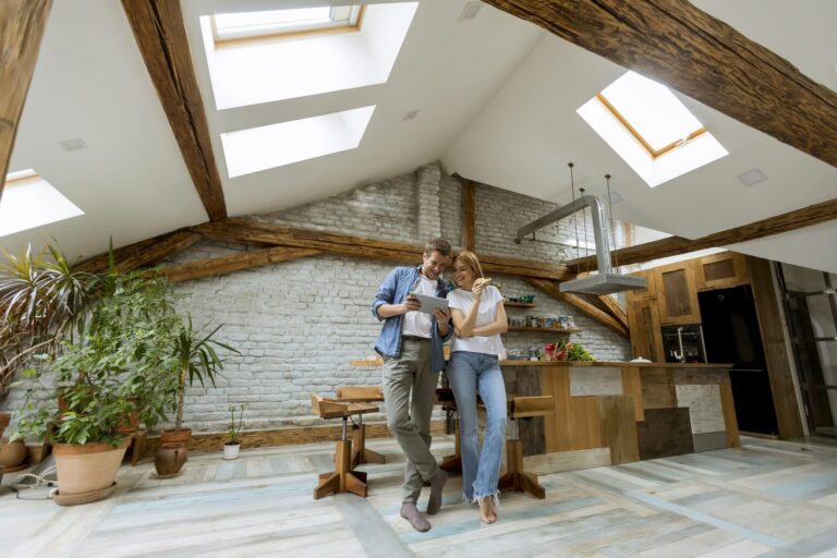 Couple in a converted loft apartment with exposed beams reviewing Leeds rental yields on a tablet