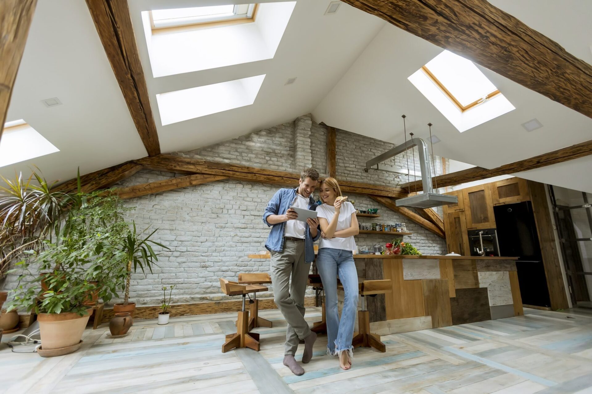 Couple in a converted loft apartment with exposed beams reviewing Leeds rental yields on a tablet