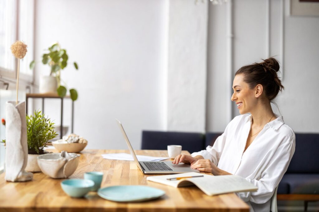 Smiling woman researching property on a laptop at a wooden dining table, representing buyers and renters in Dewsbury and Cleckheaton