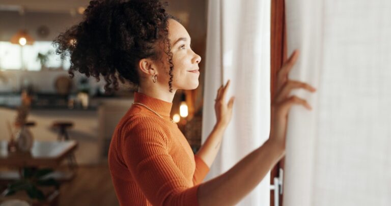 Woman looking out of a window in a warm Tamworth rental home, illustrating energy-efficiency upgrades for EPC C