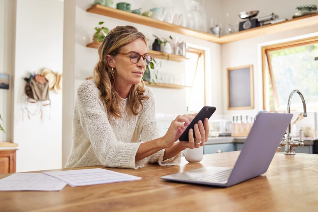 Self-managing landlord using a phone and laptop at a kitchen counter to check Renters' Rights Act requirements for a Tamworth rental