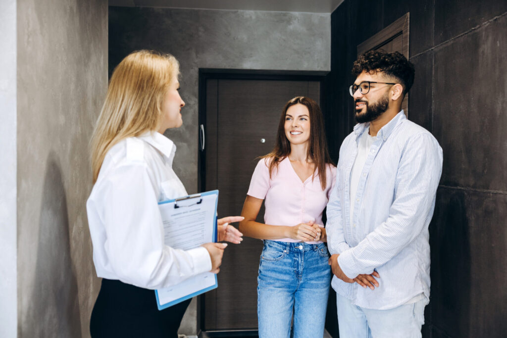 Female estate agent holding property documents while discussing a residential property with a young couple during a home viewing.