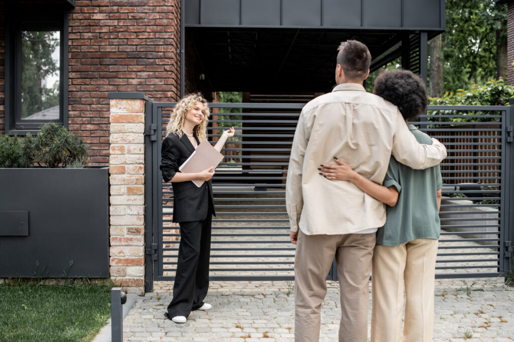 Female estate agent holding property documents while speaking with a couple outside a modern brick-built residential property.