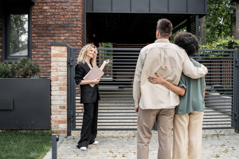 Estate agent showing a modern brick-built residential property to a couple during an outdoor house viewing.