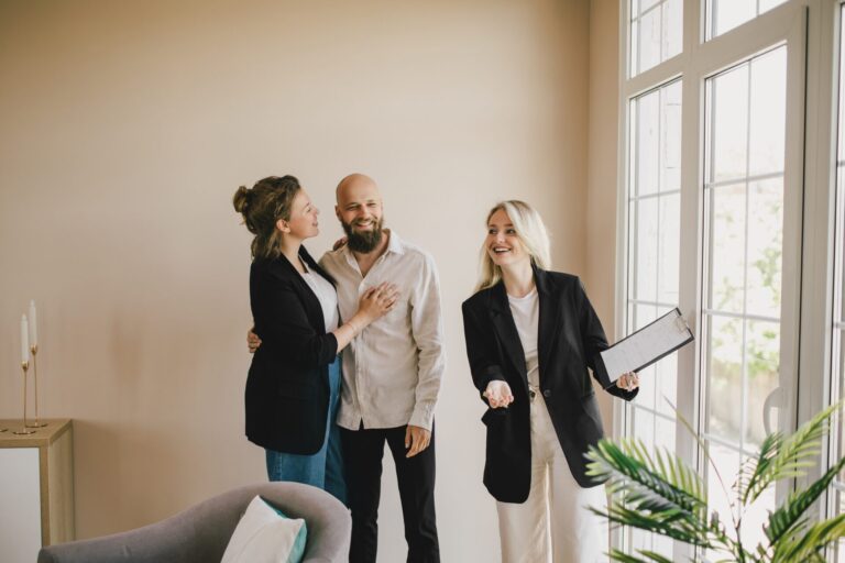 Estate agent showing a bright, modern living room to a young couple during a residential property viewing.