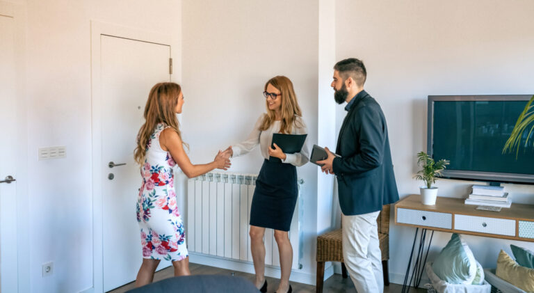 Estate agent shaking hands with a homeowner during a property consultation in a bright, modern living room.