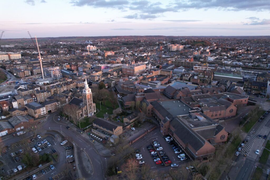 Aerial view of an urban town centre featuring a historic church, residential and commercial buildings, surrounding streets and construction cranes.